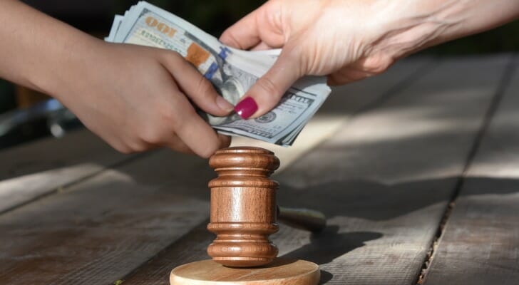 Cash being exchanged over a gavel, symbolizing payment for a lawsuit settlement.