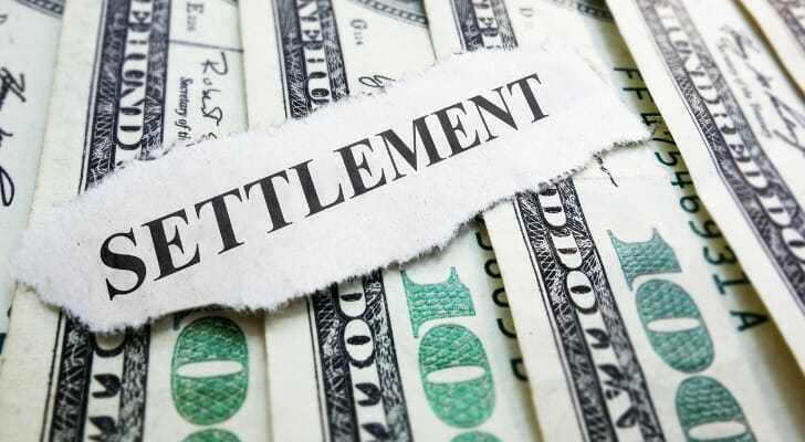 The word "SETTLEMENT" on a ripped piece of paper resting over $100 bills.