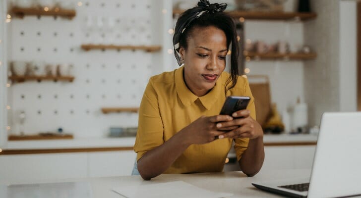 A woman on her phone, researching if closing a savings account affects your credit score.