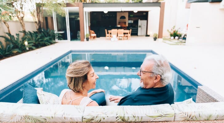 A retired couple sitting near their inground pool.