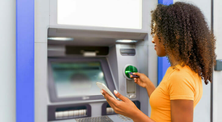 A woman following instructions on her phone for using an ATM.