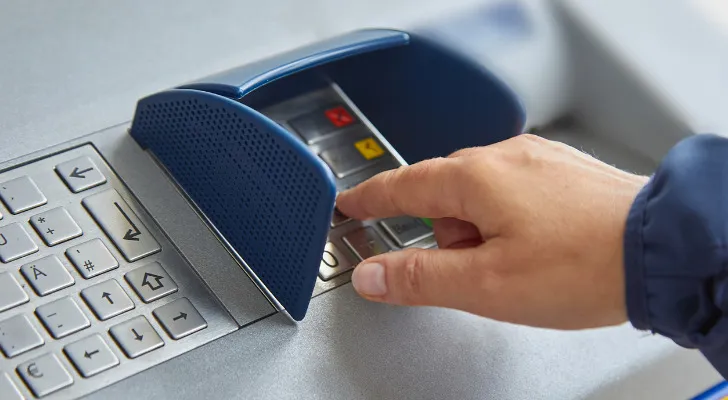Closeup of a man typing his pin into an ATM machine.