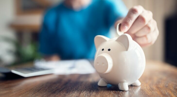 Closeup of a person putting money into a piggy bank.