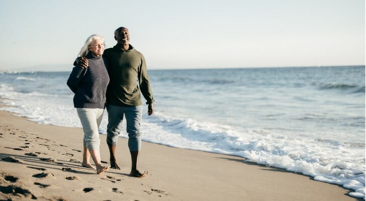 A couple walking on the beach, having retired at 55.