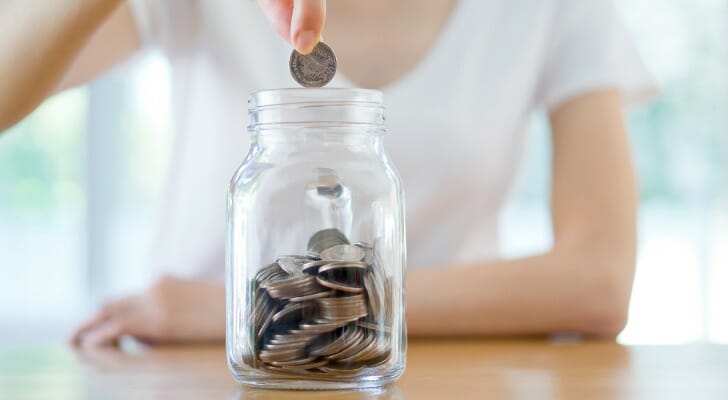 A teen putting coins into a jar.