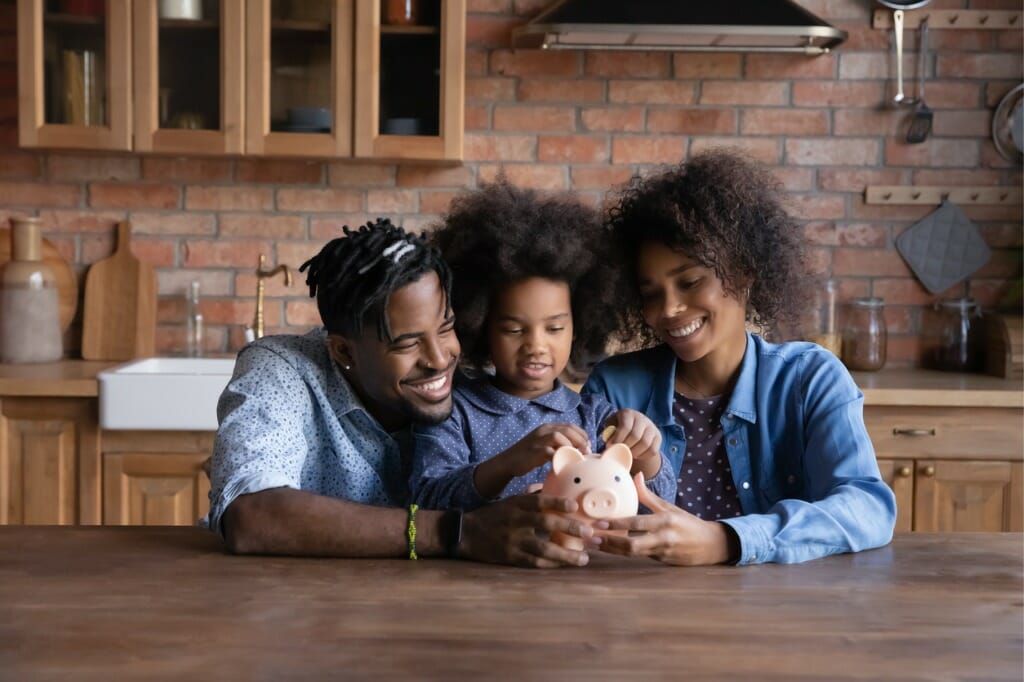 A mother and father put money in a piggy bank with their child.