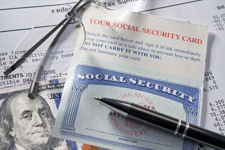 A pen and pair of glasses sit atop of a social security card and $100 bill.