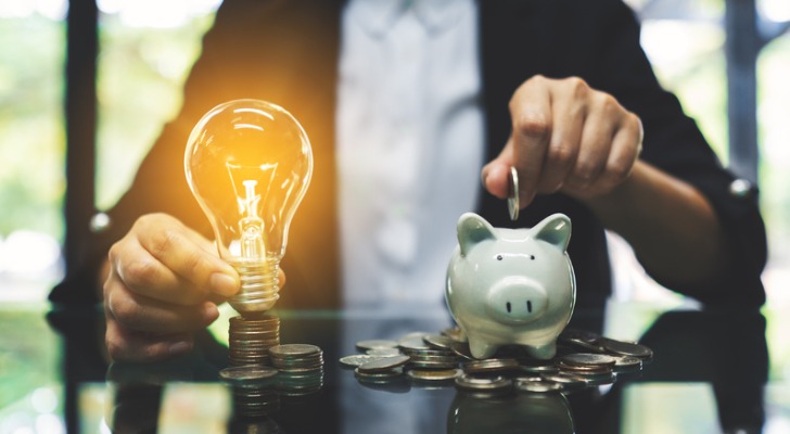 An investor holding a light bulb in the right hand and a coin over a piggy bank with the left hand to symbolize an investment opportunity.