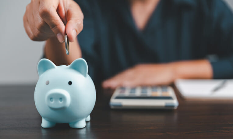 Closeup of a woman putting a coin into a piggy bank.