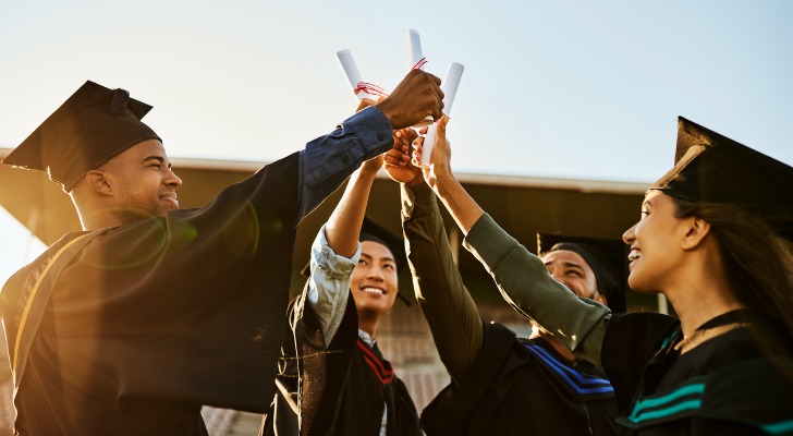 A group of college graduates celebrate by holding up their diplomas.