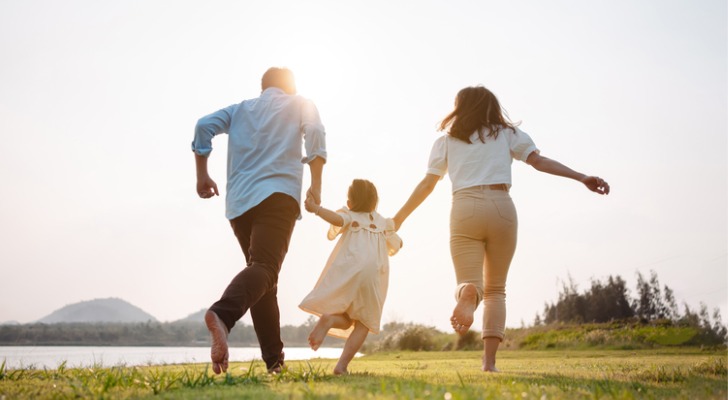 A husband and wife run beside a lake with their young daughter.