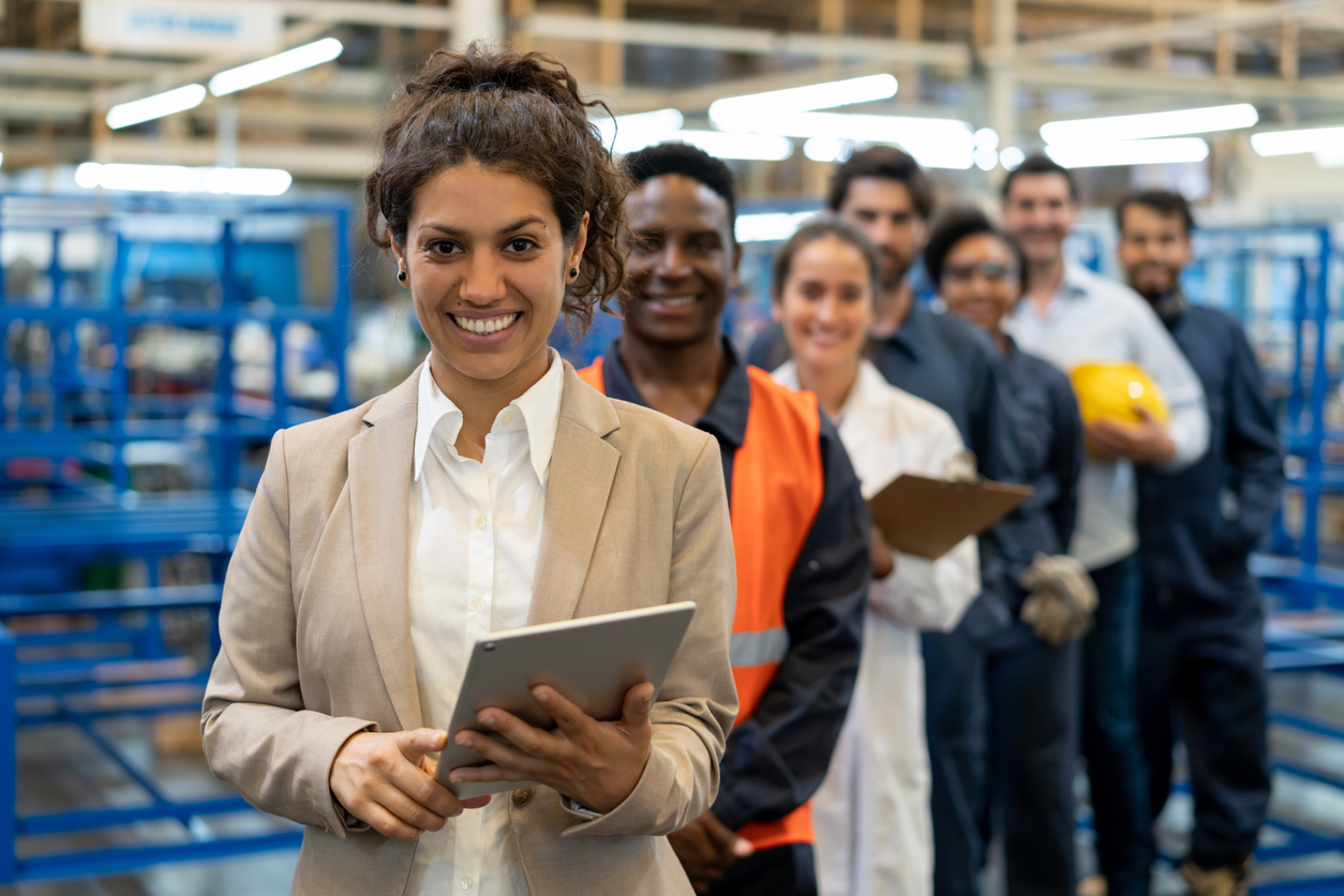A line of people in different work uniforms stand in a line in a factory.