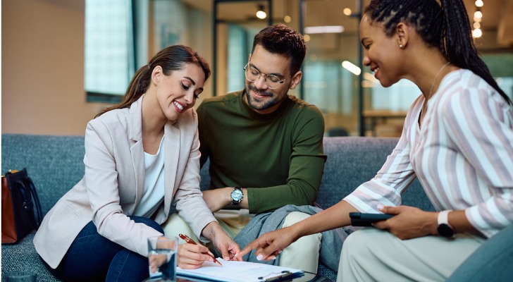 A couple signs their mortgage documents a bank employee looks on.