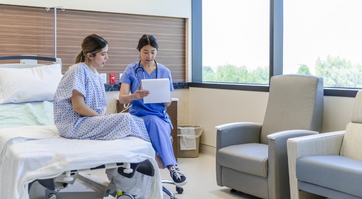A nurse sits with patient in her hospital room and asks her questions about her health.