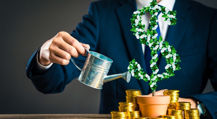 A man pretending to water an artificial plant that is shaped like a dollar sign to represent growth.