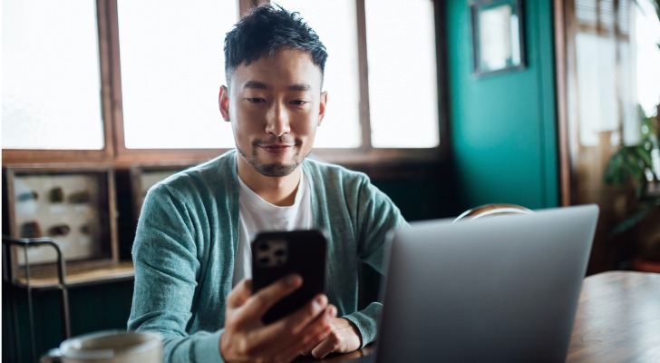 A man reviews his investments on his smartphone and laptop.