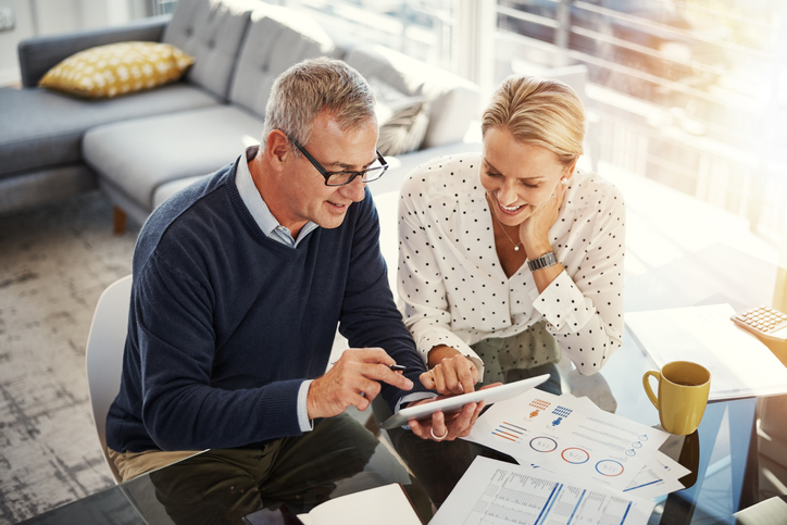 A mature couple using a digital tablet while going through paperwork at home