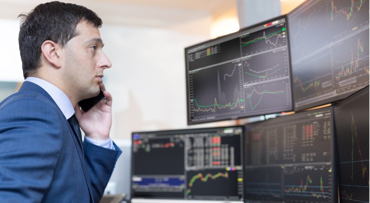 A stockbroker monitors the markets while talking on his cellphone with a client.