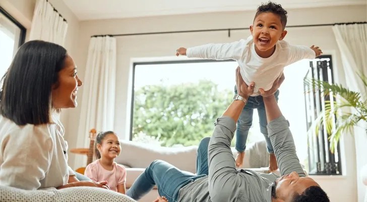 A husband and wife play with their children in the living room of their home