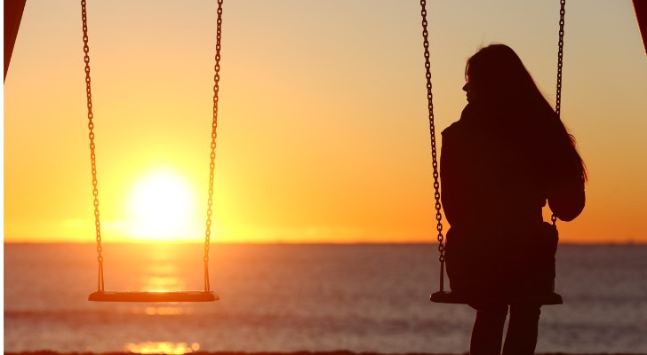 A girl who recently lost a parent sits on a swing set overlooking the ocean.