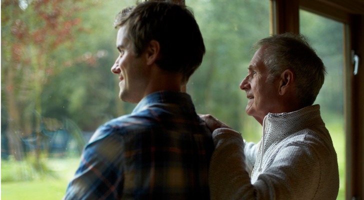 A man shares a nice moment with his son while looking out and watching his grandchildren play in the yard.