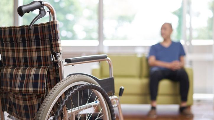 A nursing home resident sits on a couch after getting out of his wheelchair.
