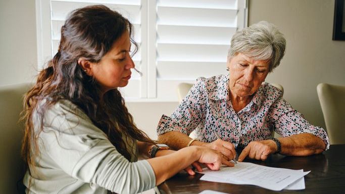 A woman signs her power of attorney form with her daughter.