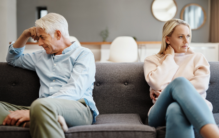 A divorcing couple turns away from each other while sitting on a couch.