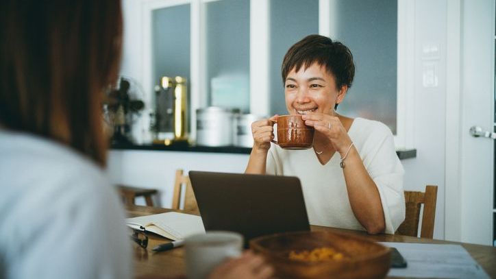A woman sips some tea while discussing retirement planning with her friend.