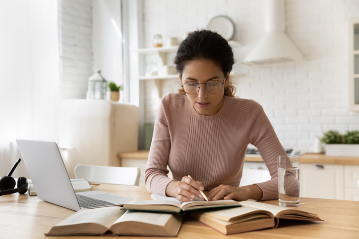 A financial advisor taking notes from multiple books as she studies for the CFP exam.