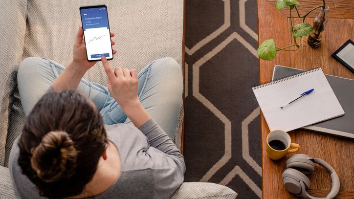 A woman purchases a stock on her cell phone from her couch.