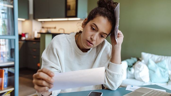 A woman holds an expired check in one hand and several overdue bills in the other.