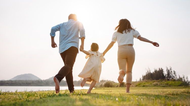 A couple plays with their young daughter beside a lake.
