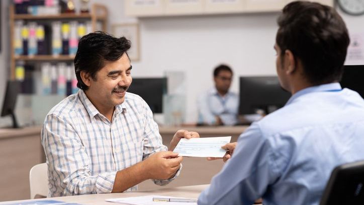 A man hands an expired check to a bank employee and asks that a new one get issued.