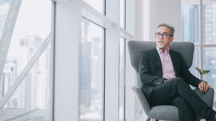 A wealthy businessman contemplates his wealth management plan from inside his office.