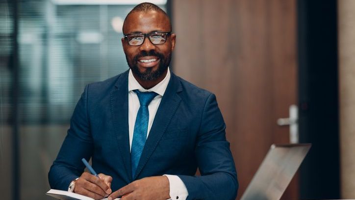 A financial advisor smiles as he takes notes on his firm's marketing strategy.