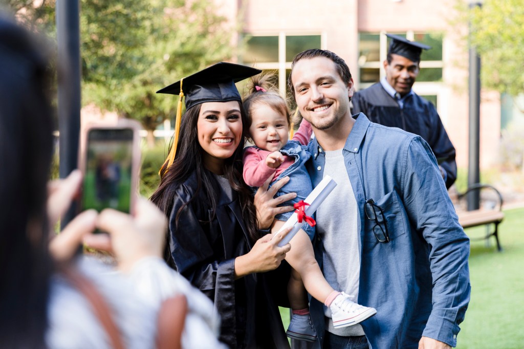 A mom posing for a picture with her child and husband at her college graduation.