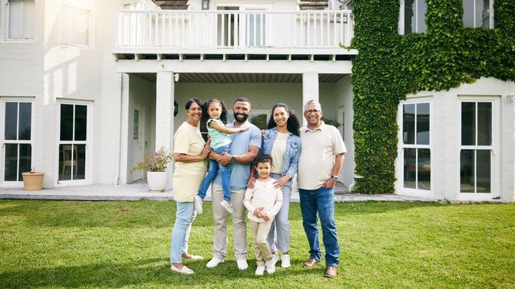 Three generations of a wealthy family stand in front of a large home owned by the family.