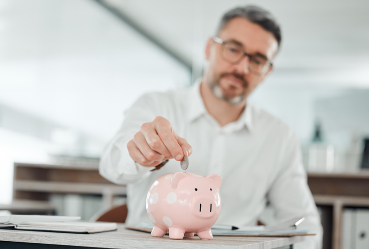 A man saving symbolically for retirement by putting a coin into a piggy bank.