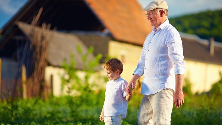 A grandfather holds his grandson's hand while walking on the grounds of the family estate.