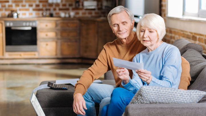 A woman looks over a Social Security check for spousal benefits with her husband.