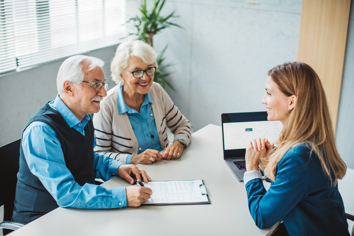 A senior couple meeting with an advisor, the wife asking, "Can I collect my husband's social security before he retired?"