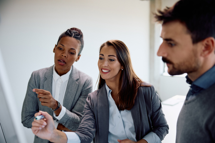 A financial advisor and her colleagues making a plan on a whiteboard for their advisory firm.