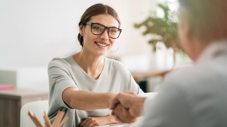 A woman in her 20s shakes hands with a financial advisor that she's considering hiring.