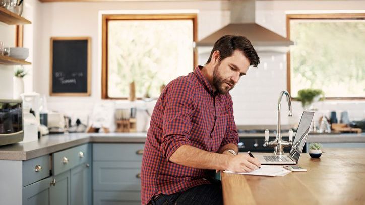 A man sits in his kitchen and lists out his short-term financial goals.