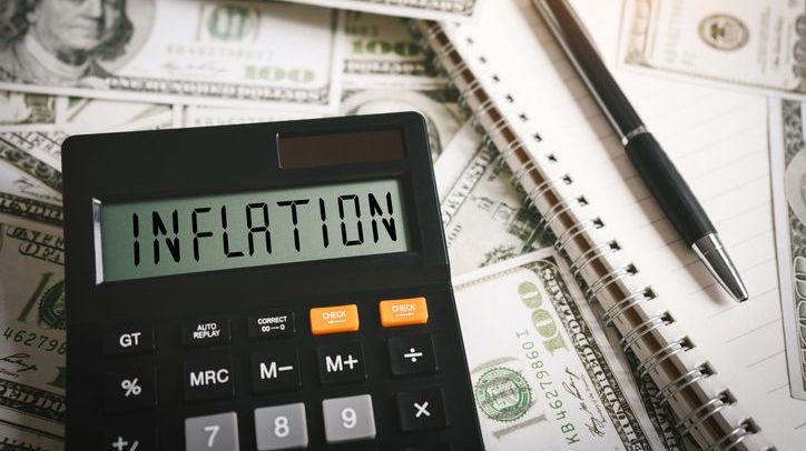 A calculator with the word "inflation" on its screen rests on top of a pile of cash.
