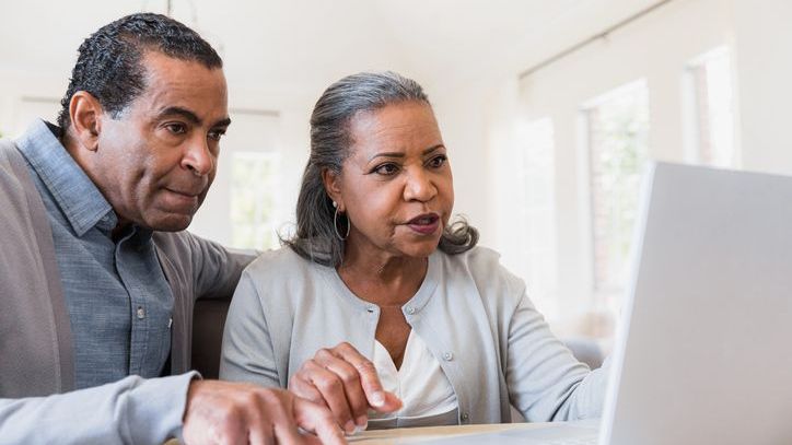 A man a woman look at a laptop screen together.