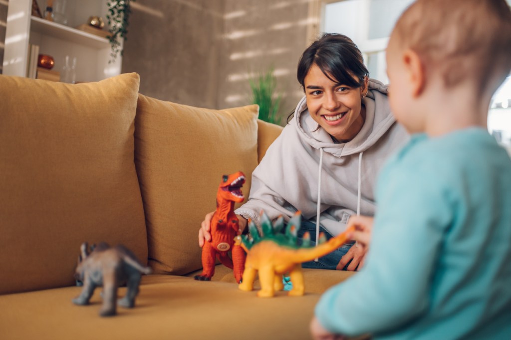 A nanny and a toddler playing with dinosaur toys.