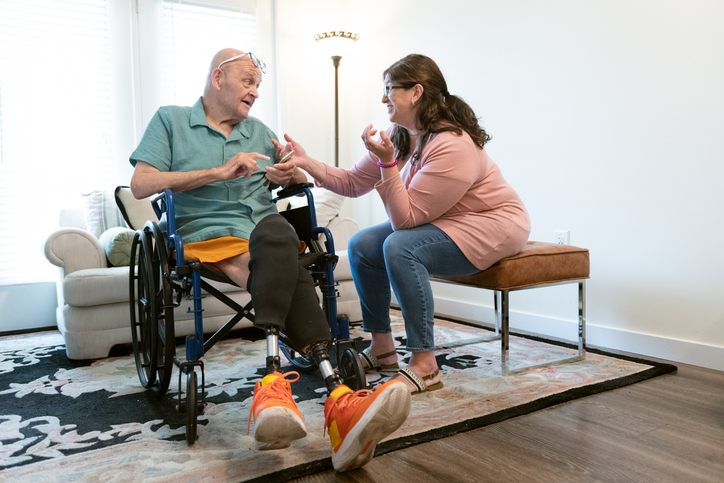 A senior man with amputations gets help from a nurse at home.