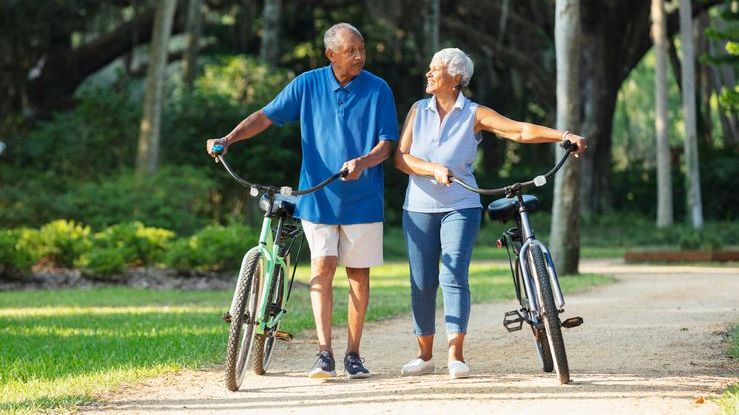 A senior couple who recently retired from their public sector jobs in Florida walk their bikes alongside each other.